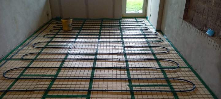 Golvvärmeinstallation med blå slangar och isoleringsmaterial, förberett på ett armeringsnät inför gjutning
